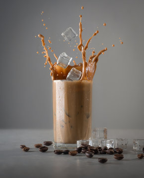 Iced coffee splash with ice cubes and beans against grey concrete