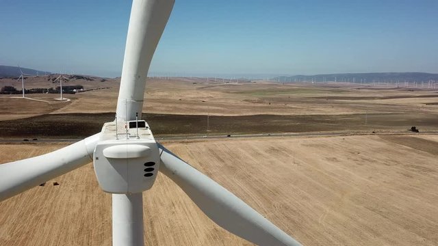Molino eolico dentro de un campo de cultivo en un dia soleado junto a la carretera grabado con dron