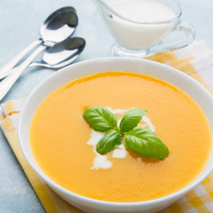 Autumn pumpkin cream soup with basil on blue table