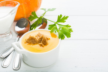 Pumpkin soup in white bowl with cream and parsley