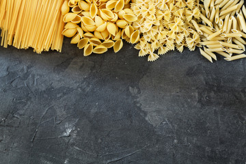 Dry pasta background. Different pasta on dark background. Flat lay. Top view.