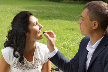 Fototapeta premium A young man is feeding his bride with grapes on a picnic in the park