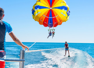 Happy couple Parasailing in Dominicana beach in summer. Couple under parachute hanging mid air. Positive human emotions, feelings, family. Young man glides on water skiing on the waves.