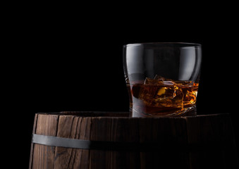Glass of whiskey with ice cubes on top of wooden barrel. Cognac brandy drink