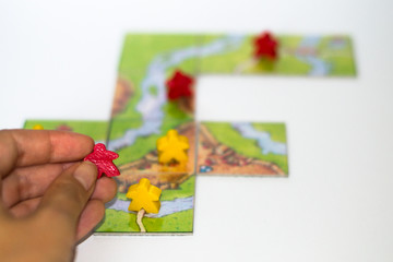 Close up red and yellow meeples in hand isolated on white background. Components of board games. Small figures of people's body in hand. Vacation time. Gameplay.