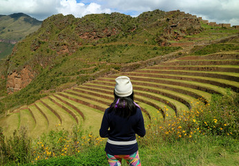 One female tourist admiring the Inca ancient agricultural terraces at Pisac Archaeological Complex, Sacred Valley, Cusco region, Peru  - obrazy, fototapety, plakaty