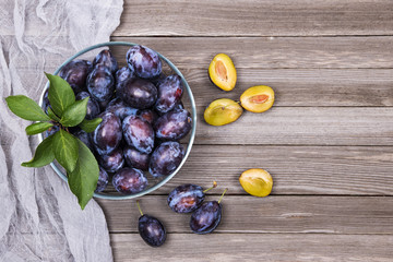 Closeup of plums in a bowl on wooden background. Top view.