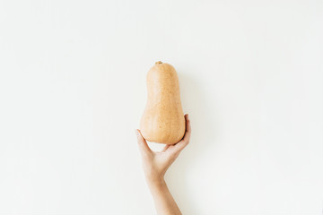 Female hand holding yellow pumpkin on white background. Fall autumn food concept. Flat lay, top view.