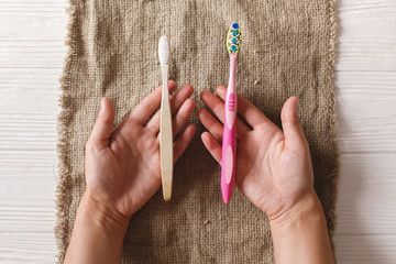 hand holding eco natural bamboo toothbrush and in other hand plastic toothbrush, flat lay on rustic...