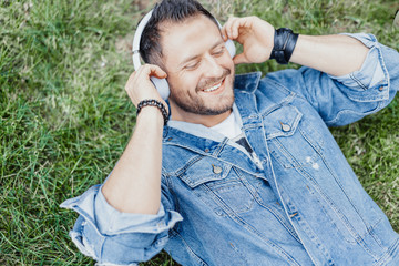 Close up of man lying on green grass and listening to music on headphones.