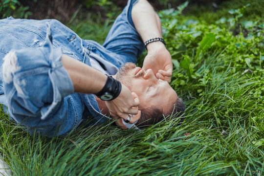 Close up of man lying on green grass and listening to music on headphones.