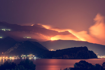 Wild fire blazing on hills above sea town.