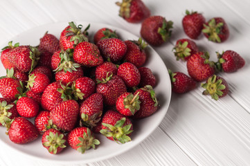 Fresh strawberries in a plate on a white wooden background.