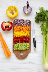 Chopped fresh vegetables (carrot, celery, red onion, colored peppers) arranged on cutting board on...