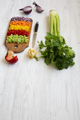 Chopped fresh vegetables (carrot, celery, onion, colored peppers) arranged on cutting board over white wooden table, side view. Copy space.