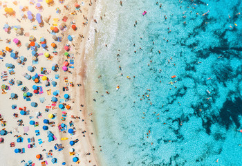 Aerial view of sandy beach with colorful umbrellas, swimming people in sea bay with transparent blue water at sunset in summer. Travel in Mallorca, Balearic islands, Spain. Top view. Landscape