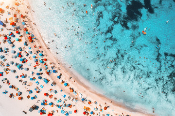 Aerial view of sandy beach with colorful umbrellas, swimming people in sea bay with transparent...