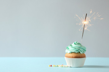 Delicious birthday cupcake with burning sparkler and space for text on light background