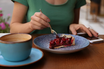 Woman eating slice of cherry cake at table, closeup
