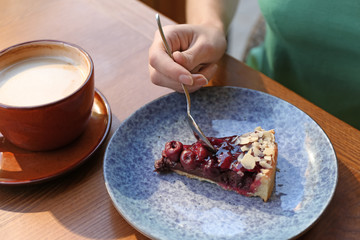 Woman eating slice of cherry cake at table, closeup