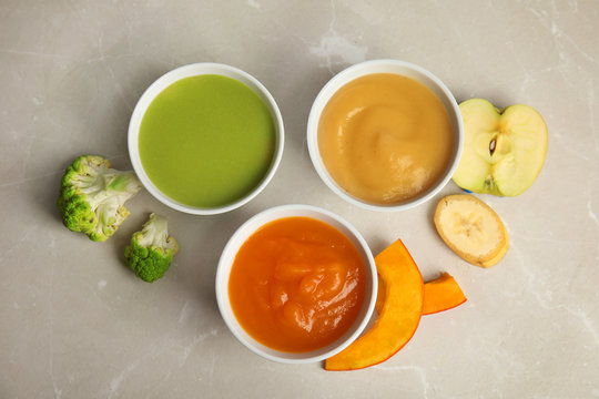 Bowls with different baby food on gray background, flat lay