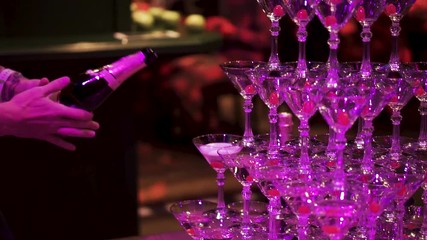 Waiter hand with glass of champagne over pyramid during catering at party. Clip. Pyramid of glasses of champagne. Champagne glasses standing in a tower at the party