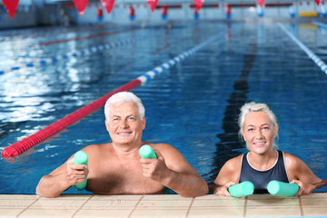 Sportive senior couple with swimming noodles in indoor pool