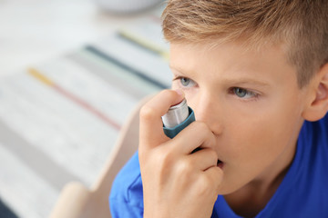 Little boy using asthma inhaler on blurred background