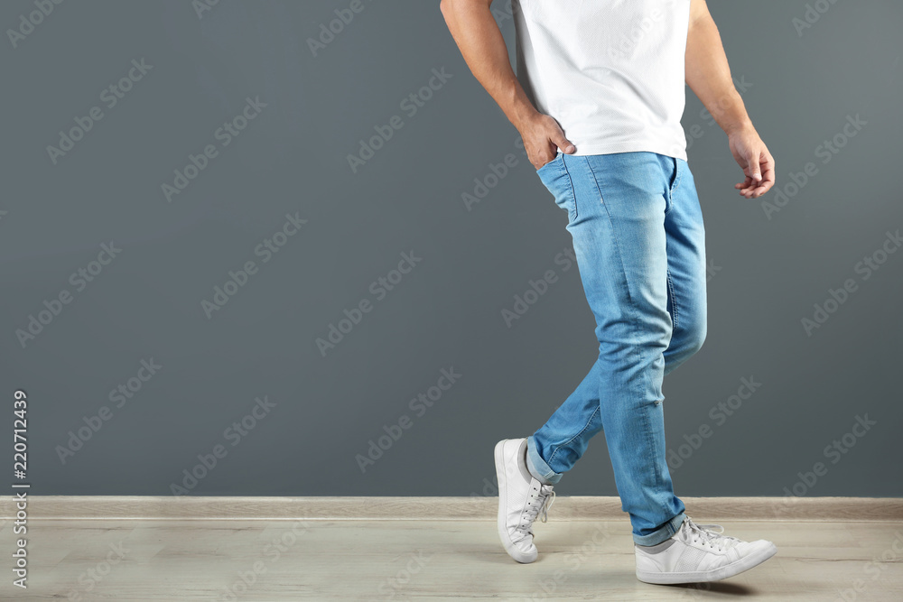 Wall mural young man in stylish jeans near grey wall with space for text, focus on legs