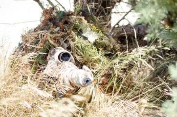 Sniper ghillie suit prone kneeling unsupported position hide in the bush scope front view outdoor