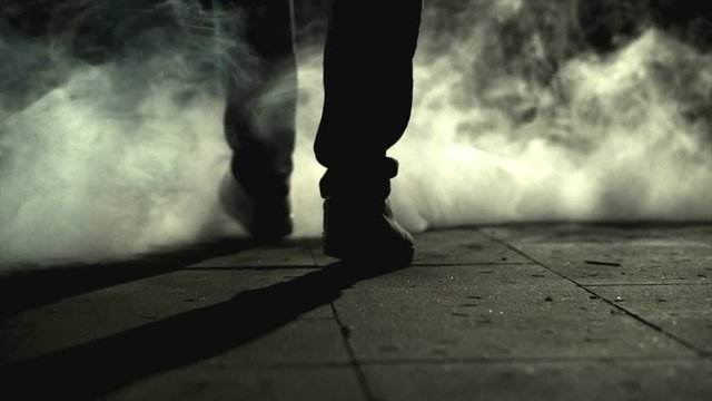 The legs of a man walking near the cloud of a smoke. slow motion