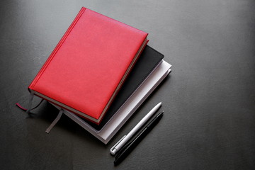 Office dark table. Mock up book blank black, red, white, leather cover for magazine, booklet, brochure, diary, business portfolio mock-up design template on black background. Flat lay, top view, copy 