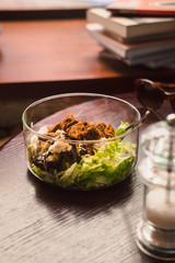 Glass bowl of healthy green salad on a dark wooden table. Low key food photography, warm tones image