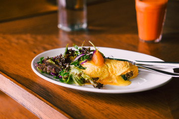 Morning breakfast, omelette with green salad on white plate with fresh orange carrot juice. Wooden table. Food photography, blogging concept.