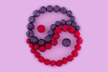 Group of berries blueberries and raspberries spread out as a Yin-Yang symbol on a light purple background.