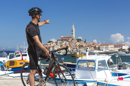Kroatien, Istrien, Rovinj, Portrait Rennradfahrer bei Pause am Hafen zeigt Richtung Sv Eufemija Kirche