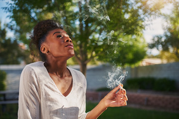 happy african american woman smoking marijuana joint in back yard
