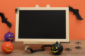 Halloween background concept. Front view of blackboard with decoration objects, pumpkin, bats, snake, spiders on orange backdrop