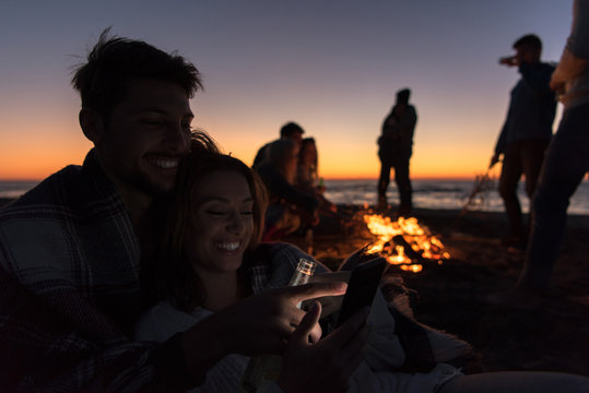 Couple enjoying bonfire with friends on beach