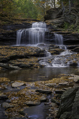 Fototapeta na wymiar Autumn Leaves Cover Rocks Surrounding a Waterfall in Ricketts Glen State Park in Pennsylvania
