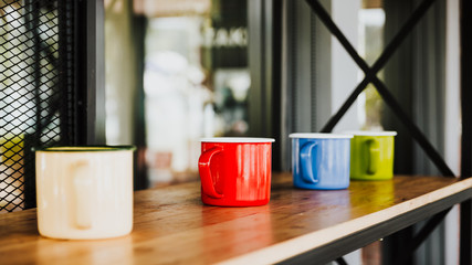 Four colorful coffee cups on wooden floor in luxury coffee shop. Focus on red cup.
