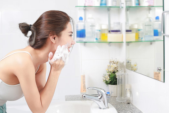 Woman happy cleanses the skin with foam in bathroom.