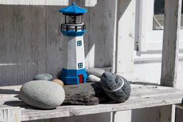 Solar lighthouse garden lamp on wooden shelf with rocks at base, nobody, summer sunshine.