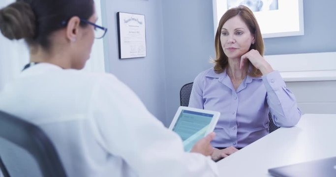 Close up of mid-aged female patient chatting with doctor indoors office setting