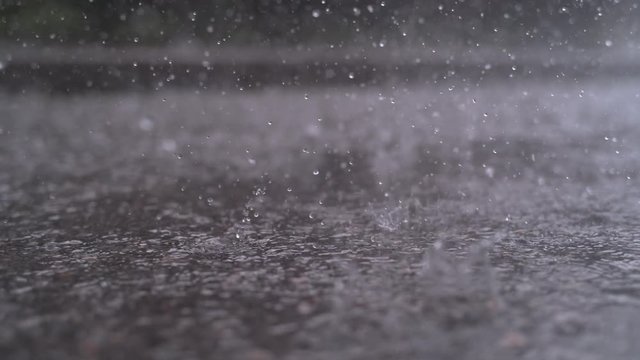 SLOW MOTION CLOSE UP: Autumn rain water drops falling into big puddle on asphalt, flooding the street. Road floods due to the heavy rain in wet season. Raindrops falling down onto submerged road