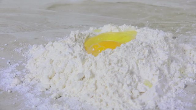 Raw egg dropping into a mound of flour on the counter top