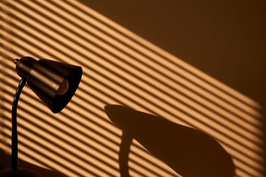 Morning sunlight coming through the window through venetian and sun-lighting a lamp and creating sunlit lamp & venetian shadow on the wall.