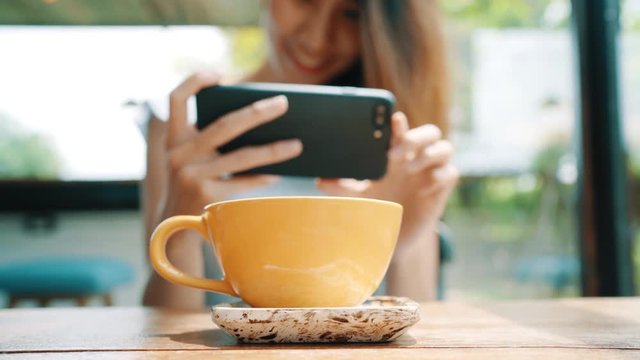 Female blogger photographing coffee cup in cafe with her phone. A young woman taking photo of coffee tea on smartphone, photographing meal with mobile camera.