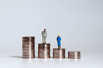 An old age miniature man and woman standing on a pile of coins.