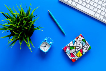 Deadline concept. Planning the day. Notebook and alarm clock on office desk with computer keyboard on blue background top view